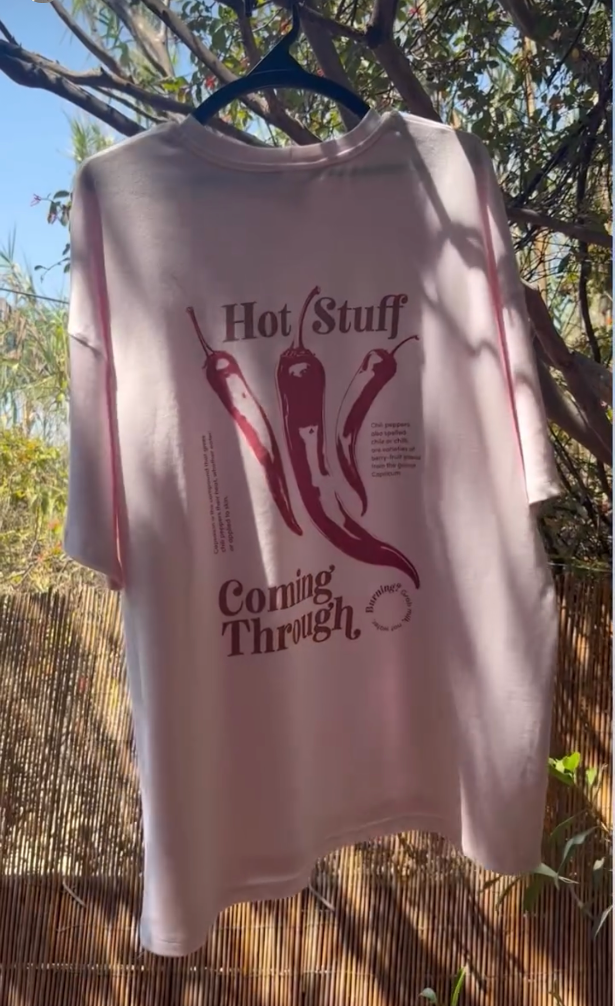 Pink t-shirt with graphic design and text hanging outdoors.