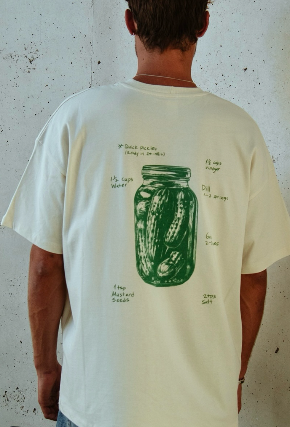 Person wearing a white t-shirt with a green graphic design on a textured wall background