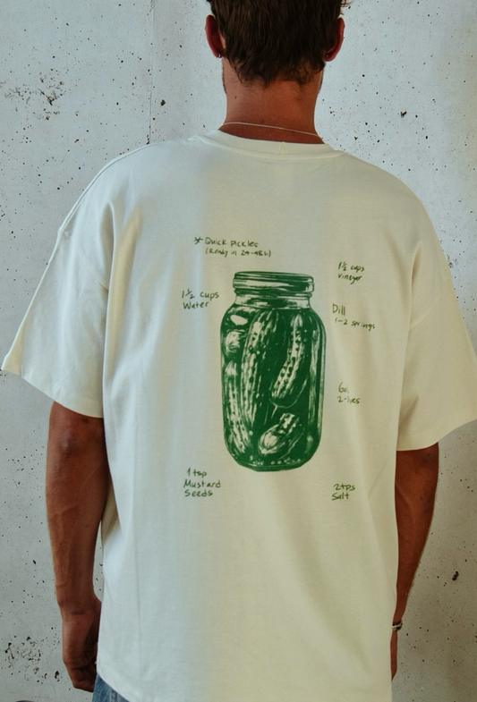 Person wearing a white t-shirt with a green graphic design on a textured wall background